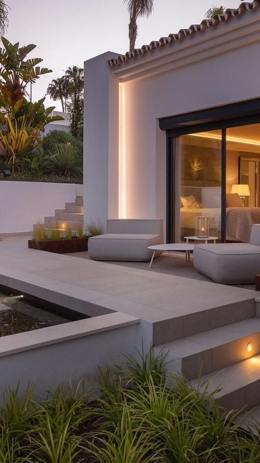Vertical twilight exterior of Villa Aquila showing planted terrace edge, seating area and warm window glow