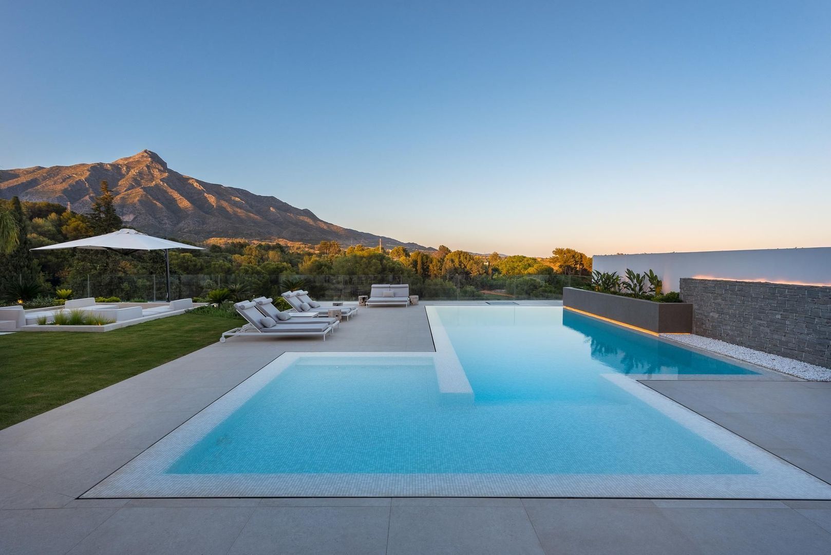Infinity-edge pool at Villa Aquila with sunrise light, water reflection and panoramic mountain view