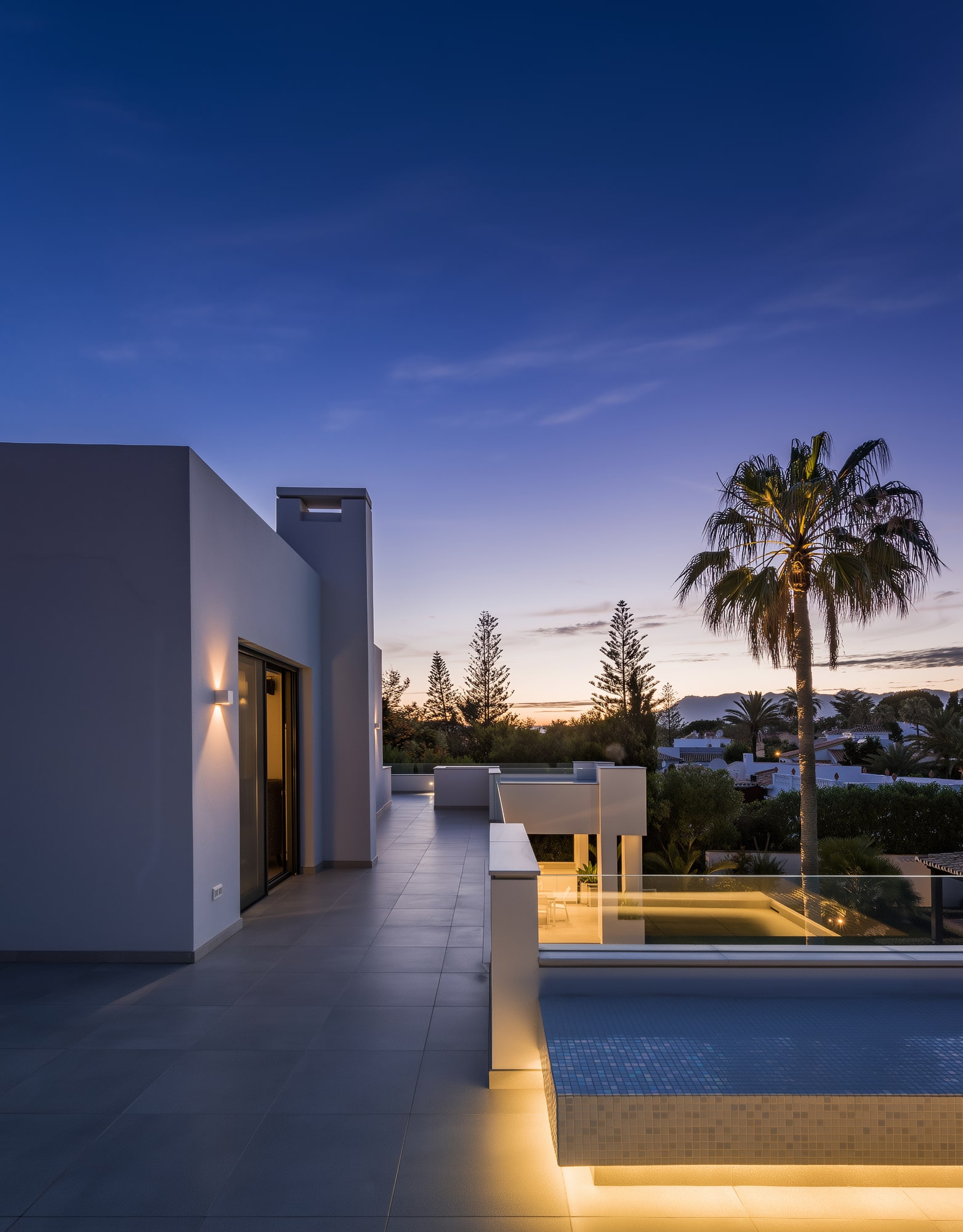 Blue-hour terrace at Villa Australia with illuminated pool edge, palms and distant Mediterranean evening horizon