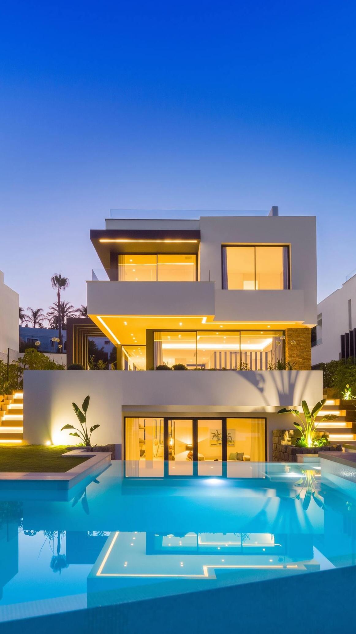 Vertical twilight view of a BELFRY villa focused on the pool edge and central illuminated façade
