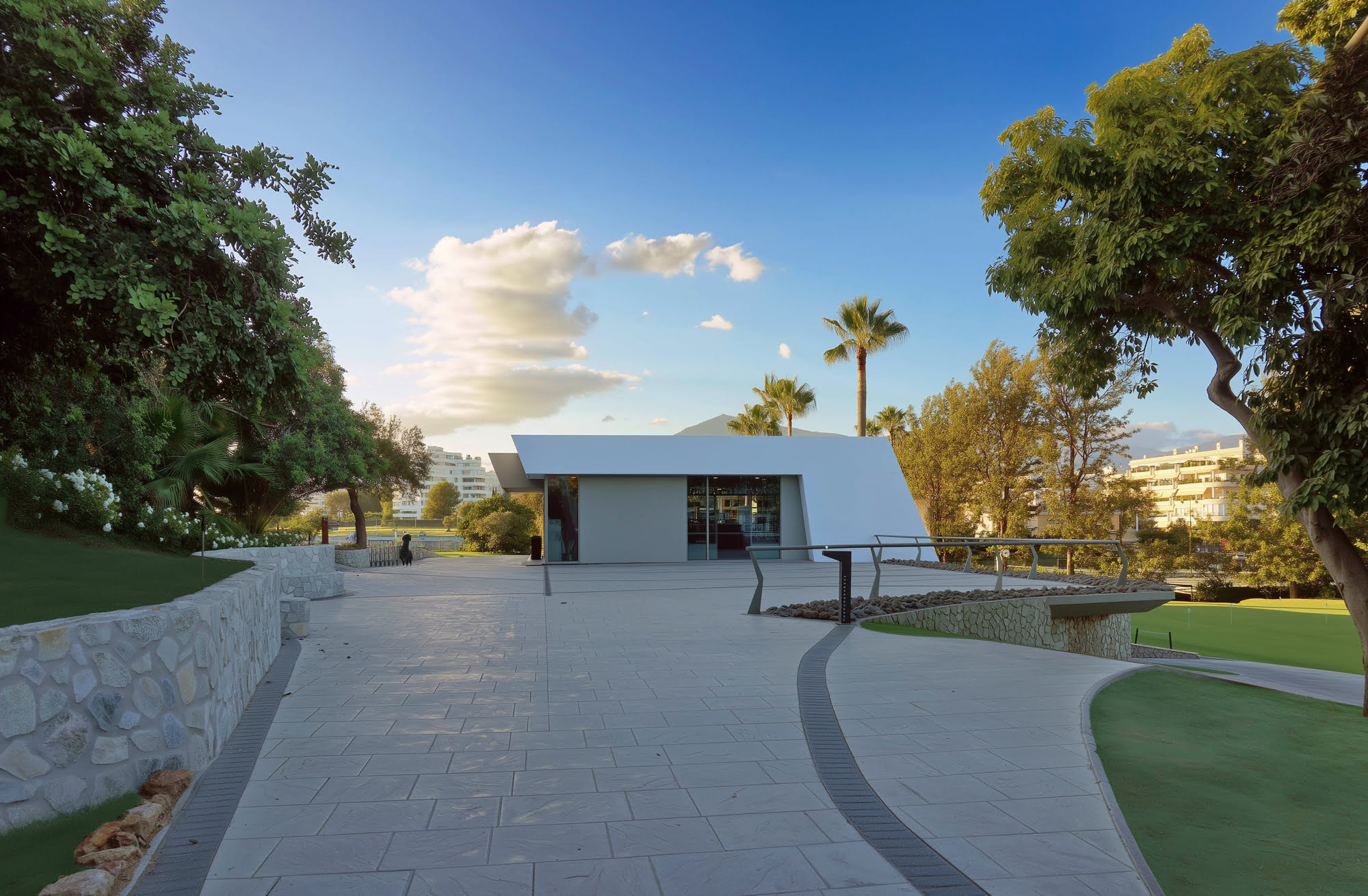 Approach view of R.C. Golf Guadalmina Clubhouse with curved driveway, lawns and sculptural white architecture in Guadalmina Alta