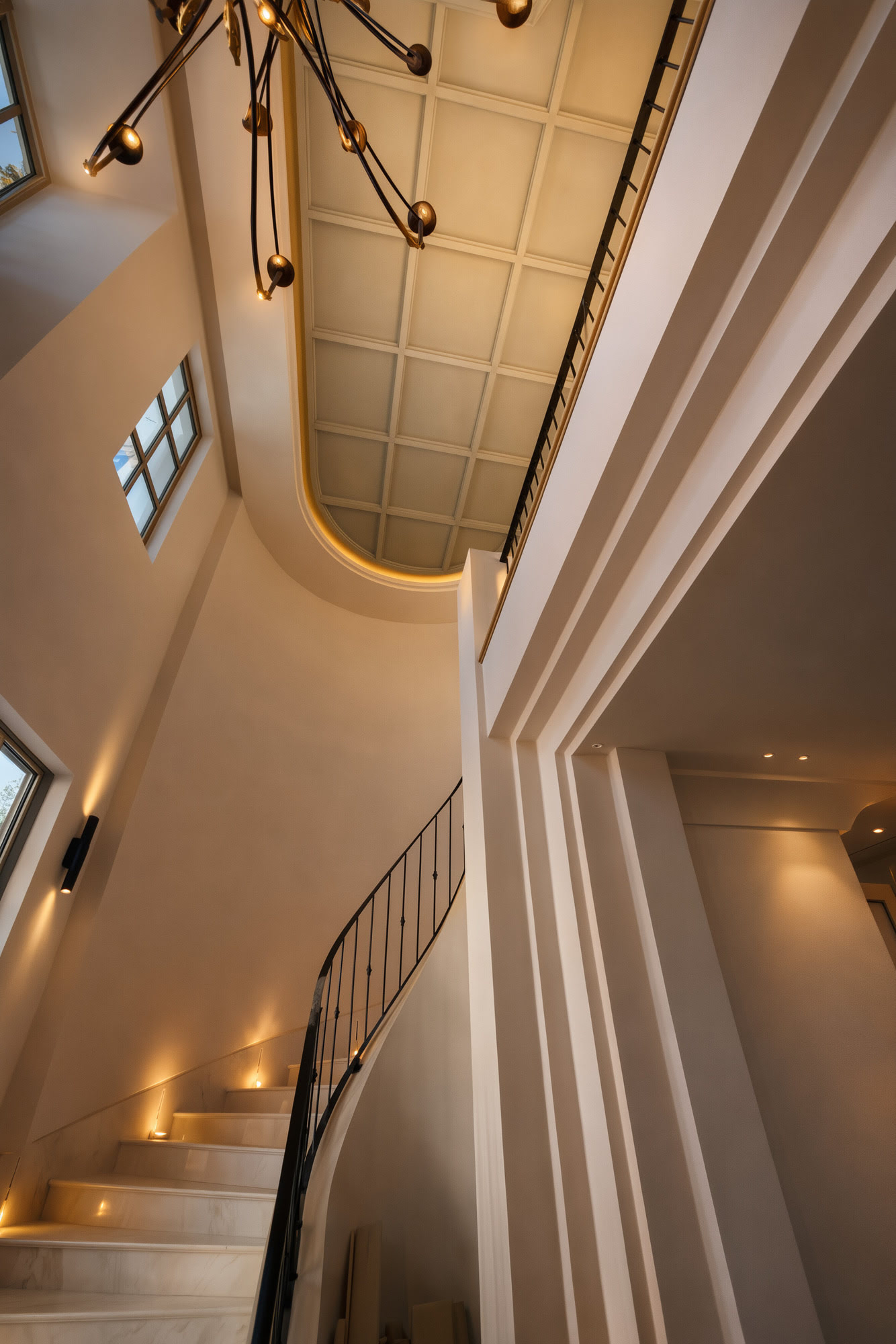 Double-height staircase sequence at Villa Diva with sculptural lines, curving soffit and warm ambient lighting