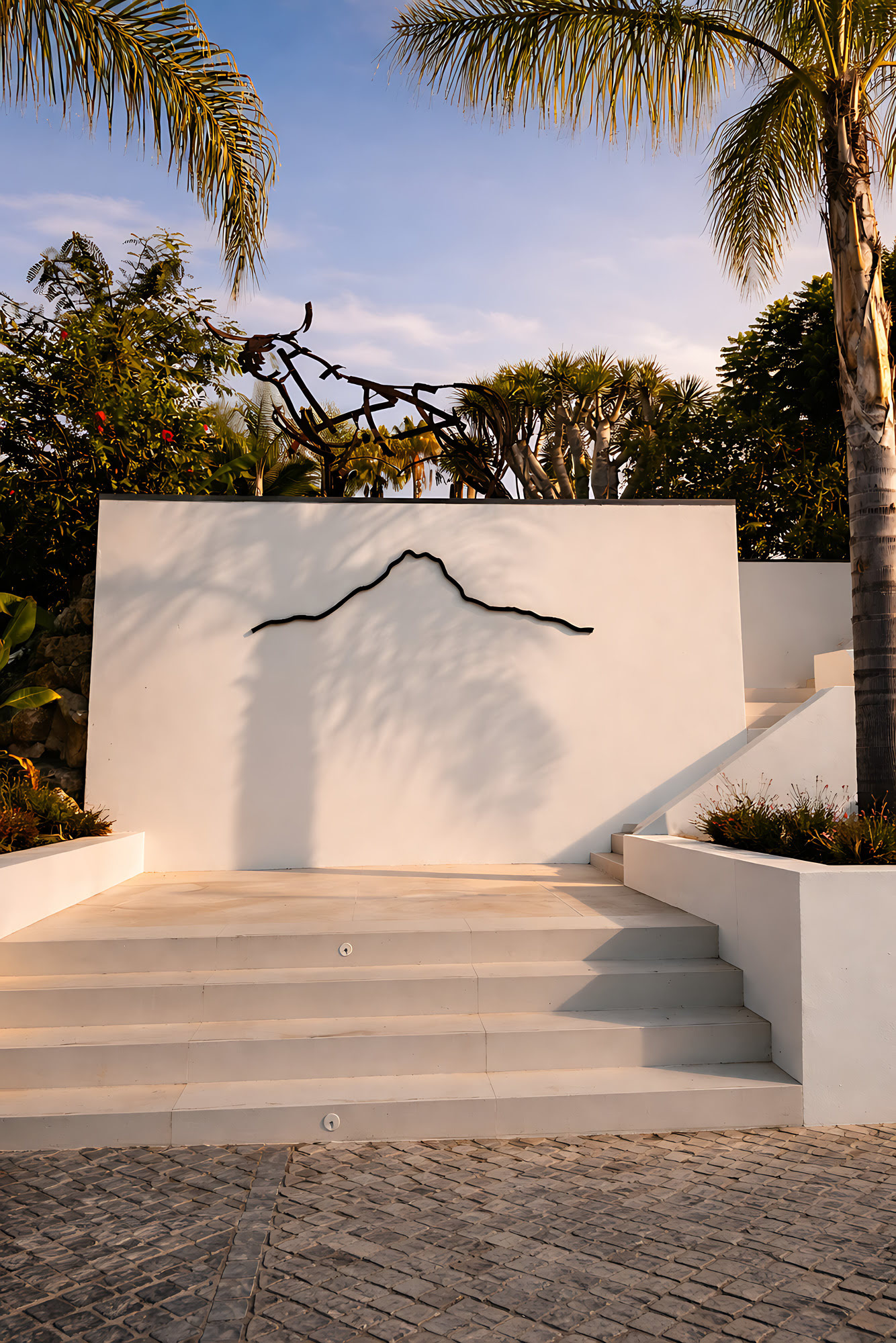 Sculptural white garden wall at Hillview Estate with integrated artwork and a calm sequence of steps and tropical planting
