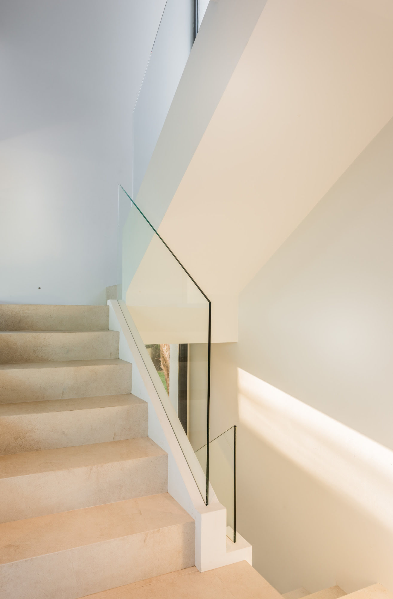 Minimal staircase at M152 with glass balustrade, pale stone steps and sculptural geometry