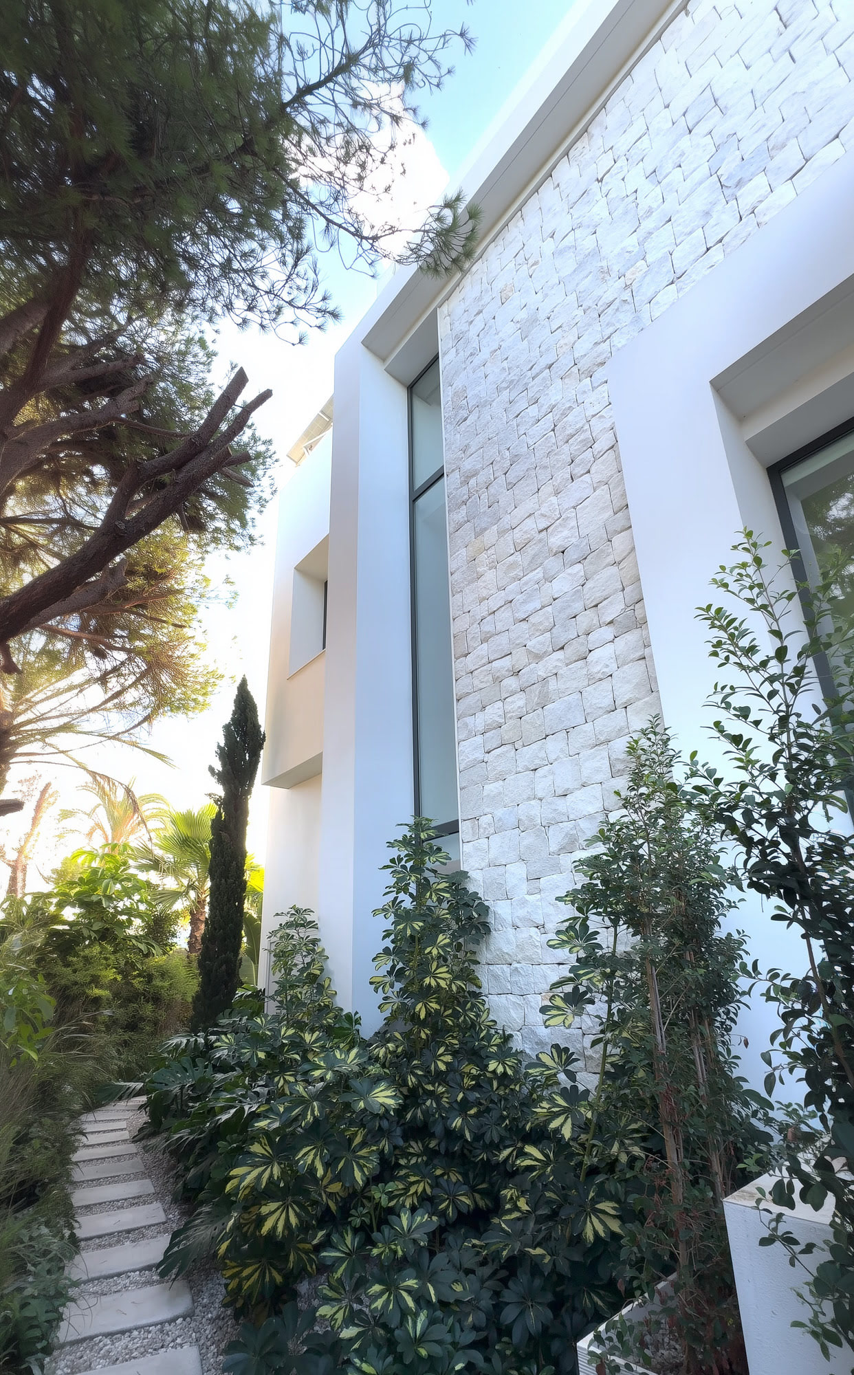 Landscaped side passage at M94 with white textured wall, stone cladding and Mediterranean vegetation
