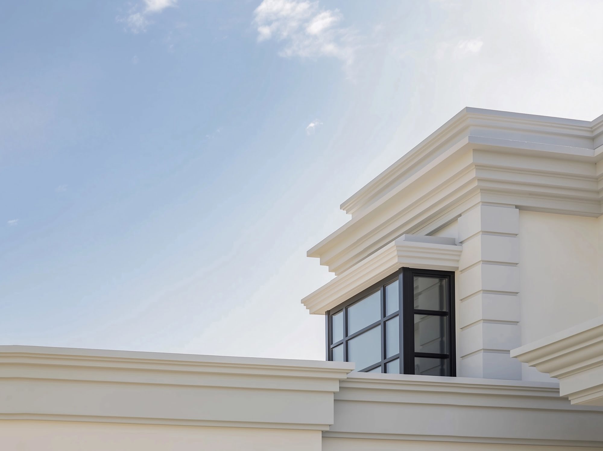 Architectural detail of the upper classical cornice and framed window at Villa Mariselena under soft Mediterranean sky