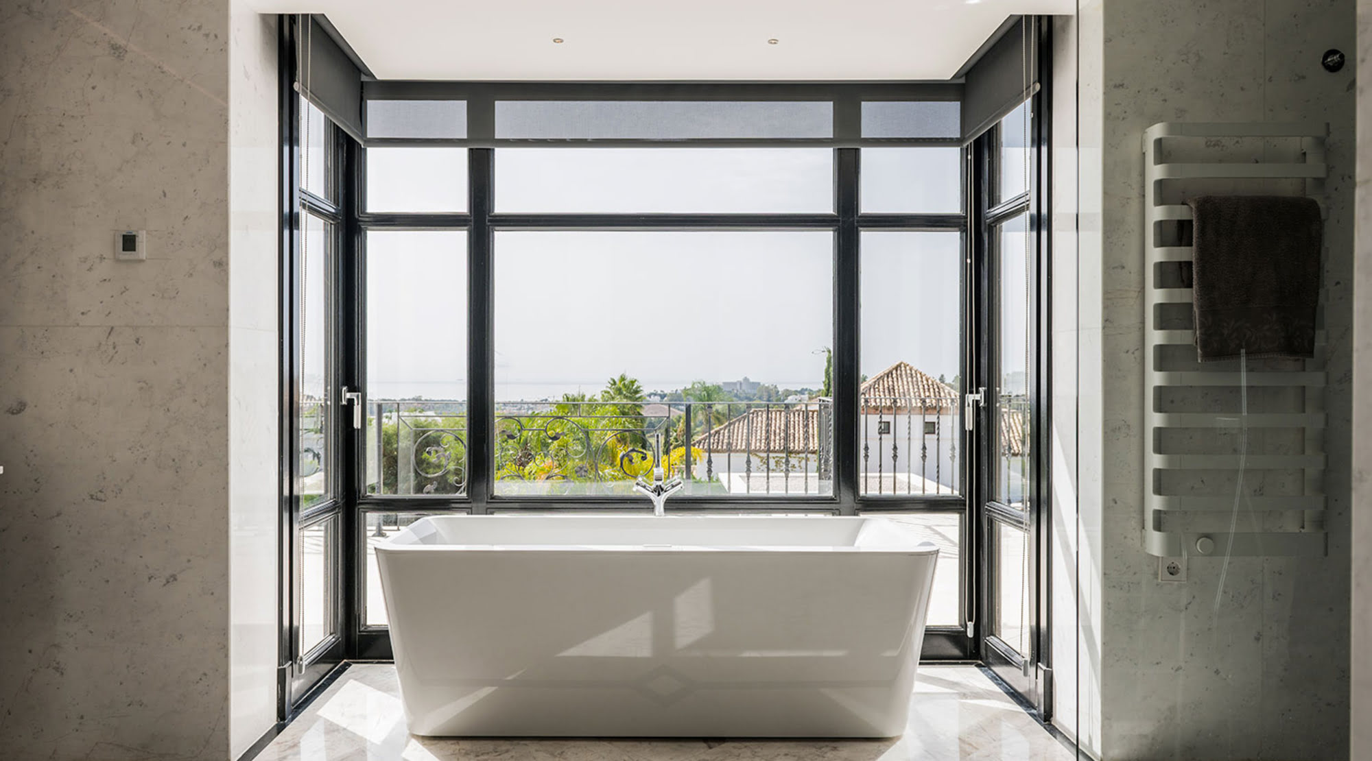 Freestanding bathtub framed by full-height glazing in the bathroom of Villa Mariselena overlooking La Zagaleta