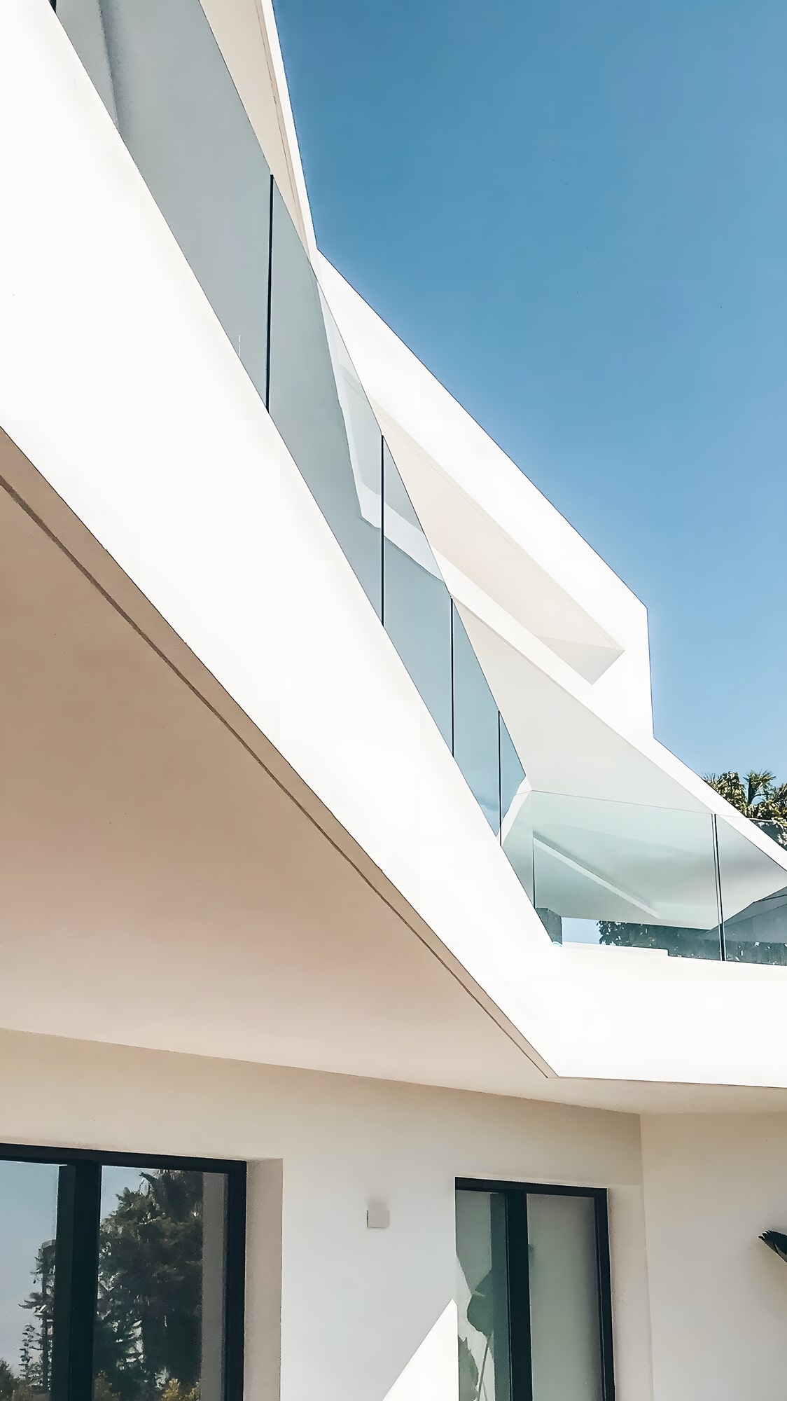 Upward view of cantilevered terraces and glass balustrade at Villa Origami against a clear sky
