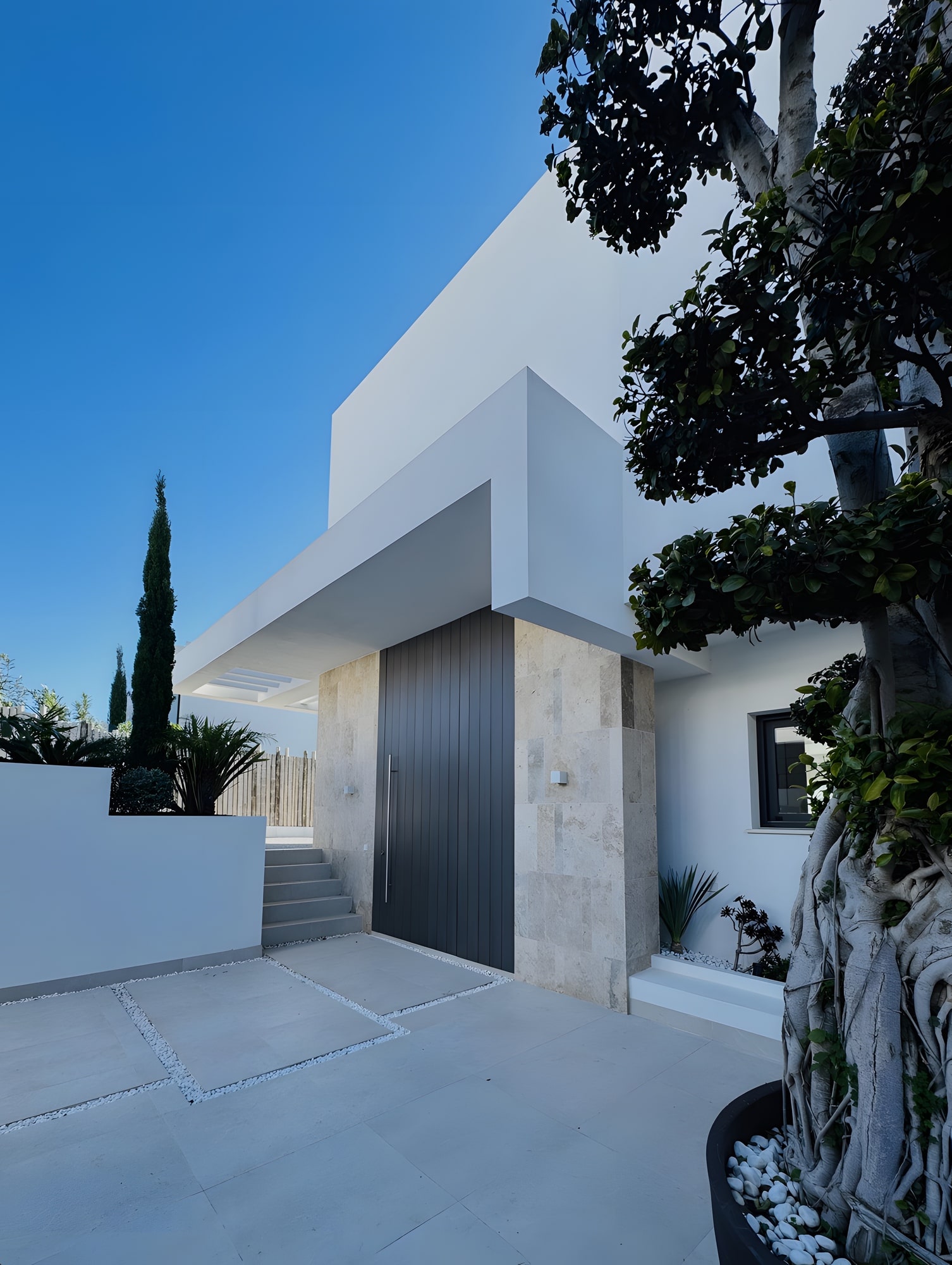 Entrance court framed by white walls, planting and a restrained Mediterranean material palette