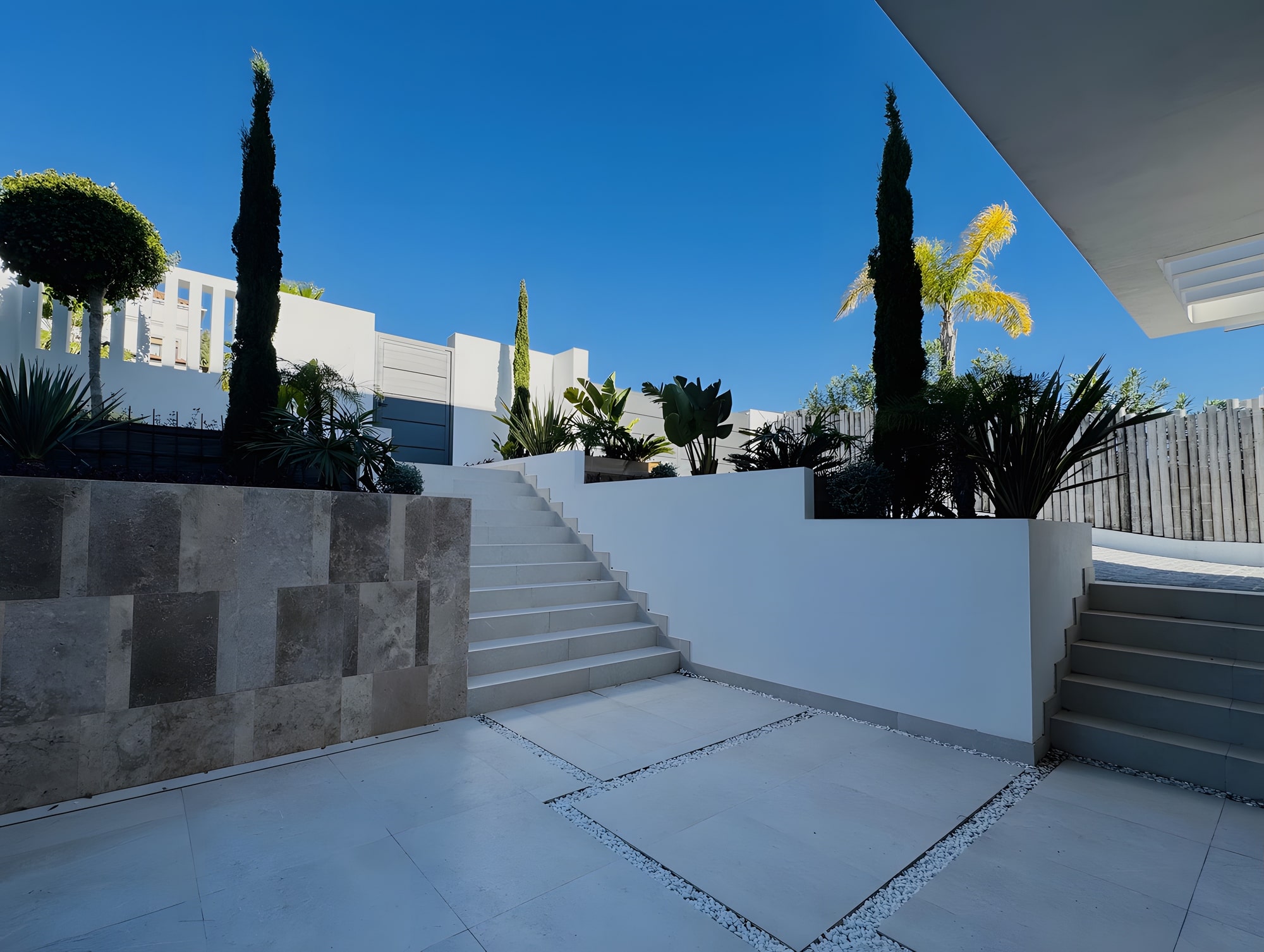 Terraced exterior approach with stone retaining walls, cypress planting and geometric white architecture