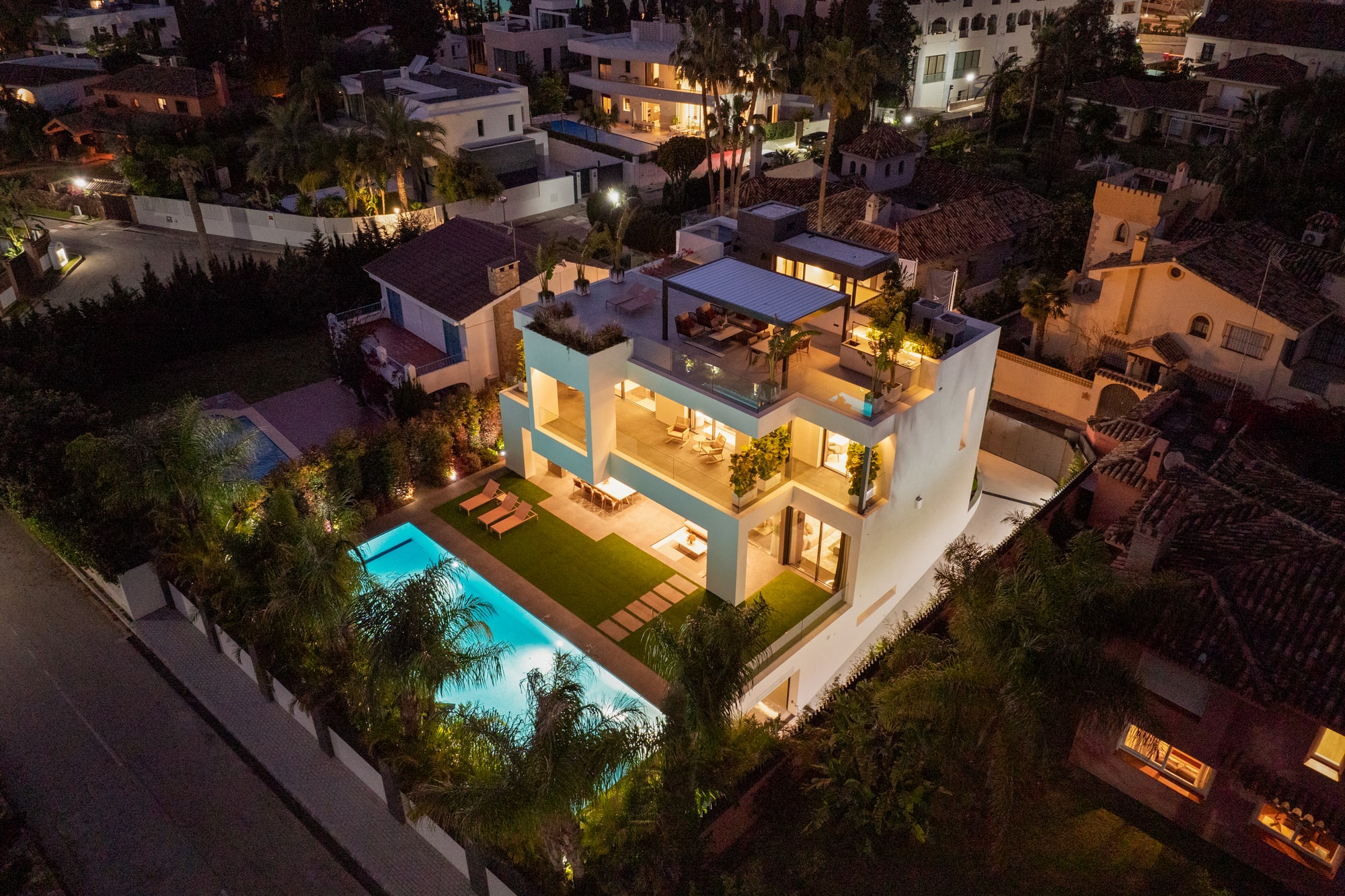 Aerial twilight view of Casa Velázquez on the Marbella Golden Mile with illuminated pool, roof terraces and landscaped surroundings