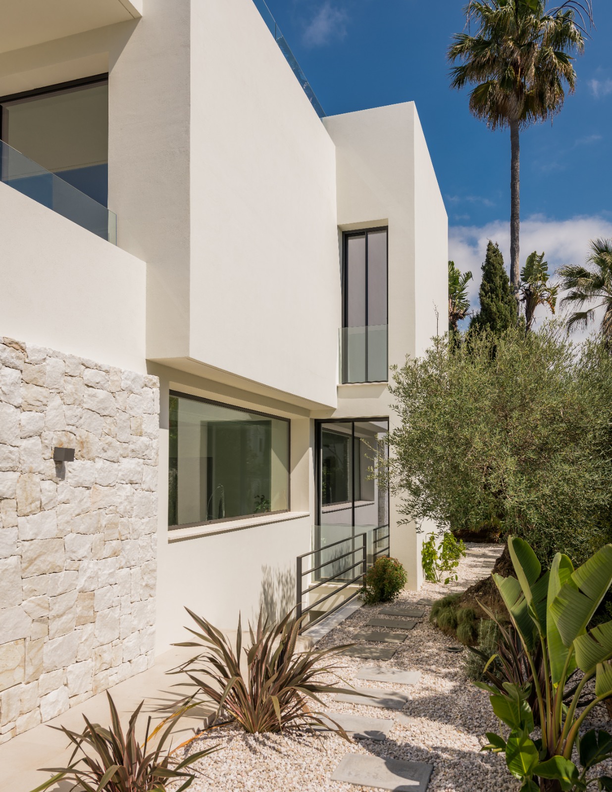 Side architectural view of VIDA DEL MAR showing textured stone walls, white volumes and garden pathway