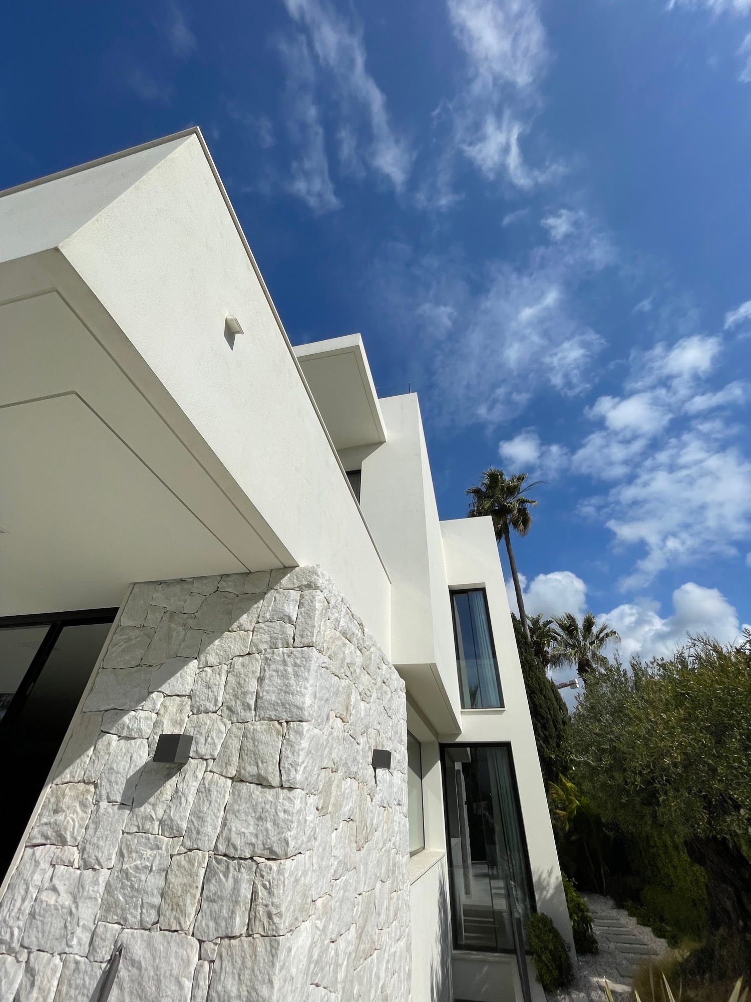 Upward perspective of VIDA DEL MAR emphasising cantilevered rooflines, stone cladding and Mediterranean sky