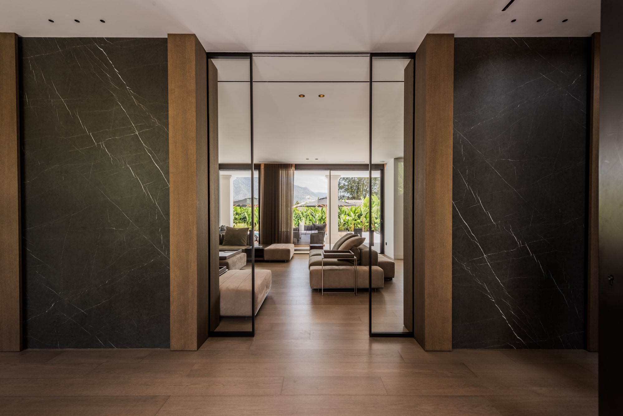 Entrance hall of Villa Zarina with tall pivot doors, natural stone flooring and a framed view through the interior axis