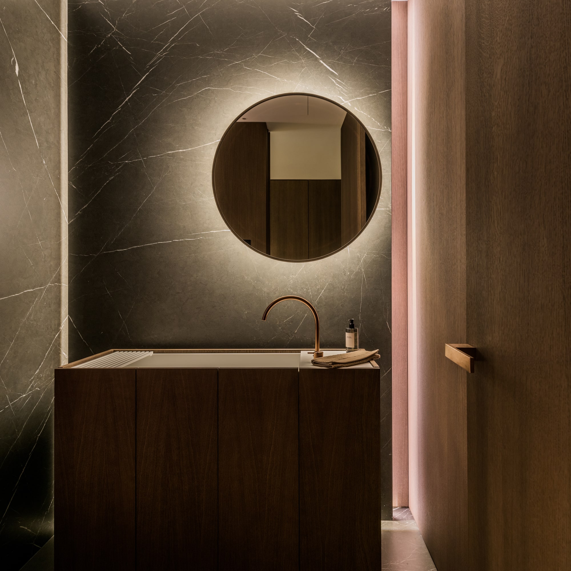Guest powder room at Villa Zarina with circular mirror, dark stone surfaces and warm concealed lighting